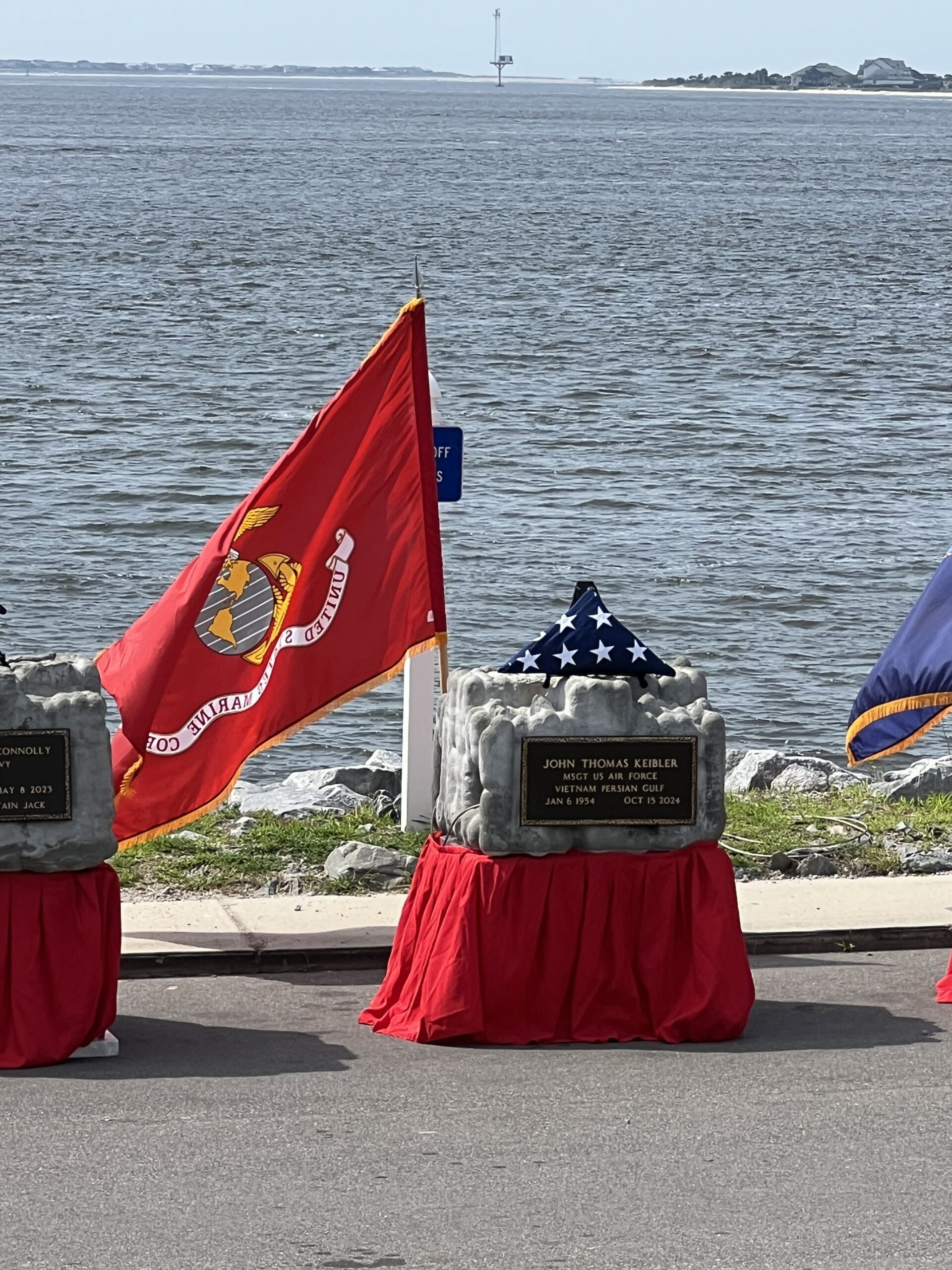 Memorial markers and military flags arranged beside the water for a commemoration